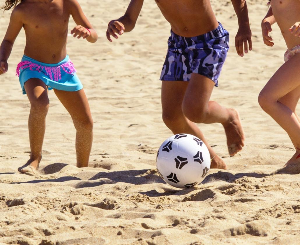 Bambini giocano a calcio sulla spiaggia, divertendosi sotto il sole estivo.