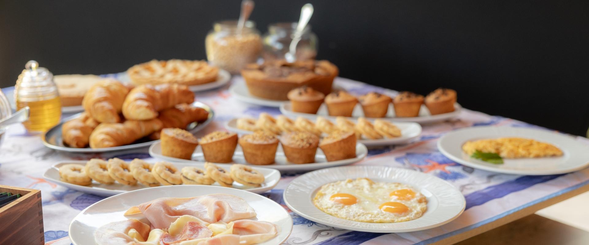 Colazione con croissant, uova fritte, muffin, salumi e dolci su un tavolo apparecchiato.