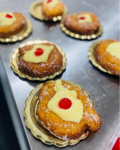 Dolci fritti con crema pasticcera e ciliegia, serviti su vassoi dorati.