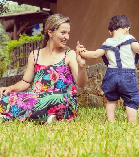 Donna seduta sull'erba tiene la mano di un bambino che cammina.