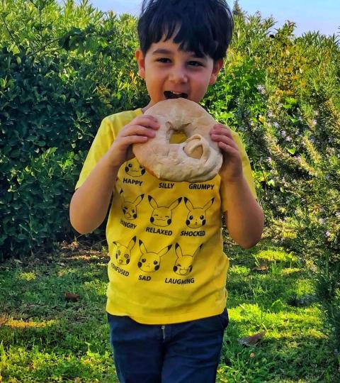 Bambino mangia un grande pane, indossa maglietta gialla con facce di Pikachu.