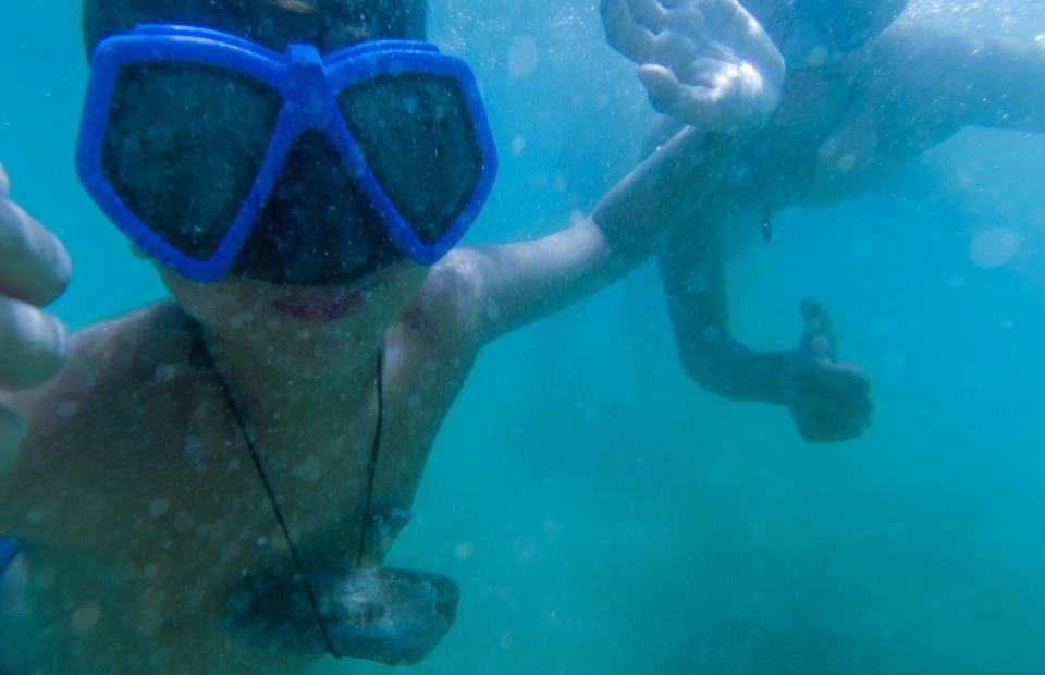 Due persone nuotano sott'acqua con maschere, facendo un gesto di OK.